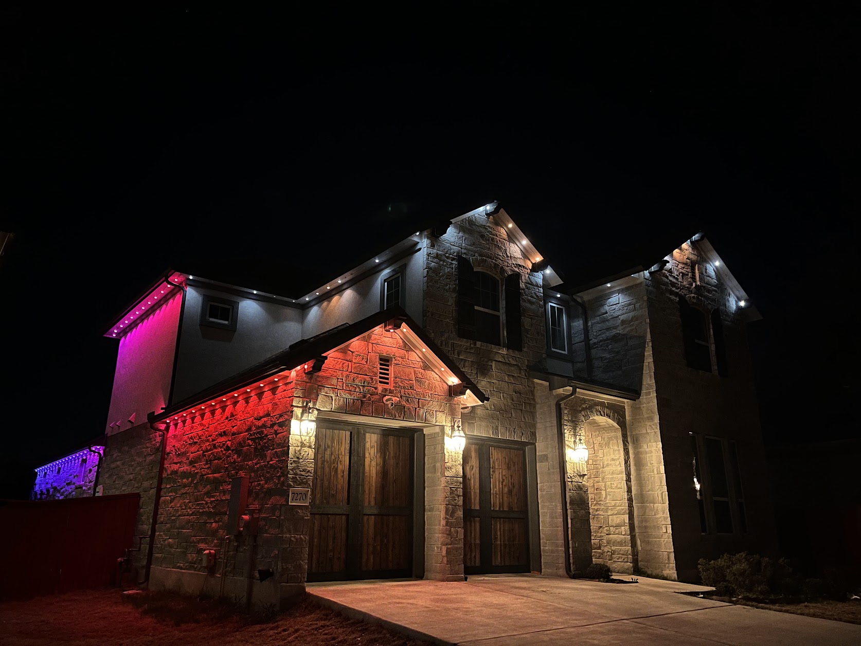 Govee permanent outdoor lights in red and warm white on a stone house installed by Fokins near Austin TX